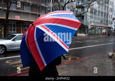 Une personne attend à un arrêt de bus londonien tenant un parapluie drapeau de l'Union Banque D'Images