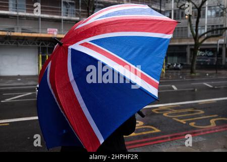 Une personne attend à un arrêt de bus londonien tenant un parapluie drapeau de l'Union Banque D'Images