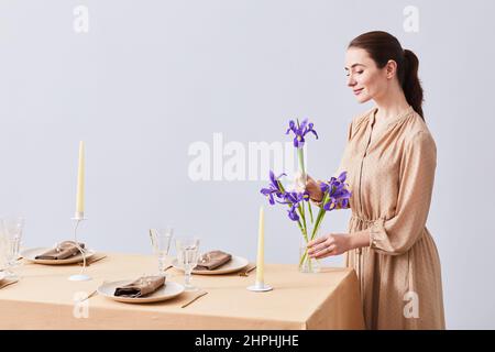 Portrait minimal de la jeune femme décorant la table de dîner avec les élégantes fleurs de l'iris pour le printemps, espace de copie Banque D'Images