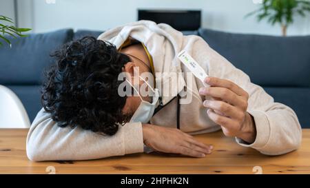 Un homme caucasien triste fait un appareil de test rapide à domicile pour Covid19 virus avec un résultat positif et tenant sa tête à la main à la table en bois. antigène actif Banque D'Images