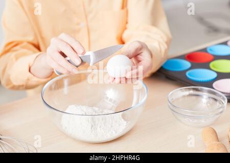Gros plan de la jeune femme cassant des œufs tout en faisant cuire des muffins faits maison dans la cuisine, espace de copie Banque D'Images