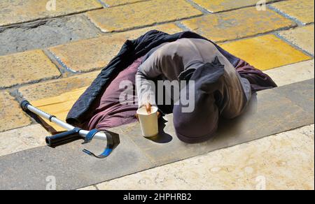 Une femme vêtue de noir avec une béquille supplie les almes qui se trouvent sur les escaliers en Europe Banque D'Images