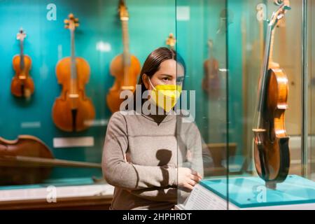 Visiteur de musée féminin dans le masque examinant les instruments de musique anciens Banque D'Images