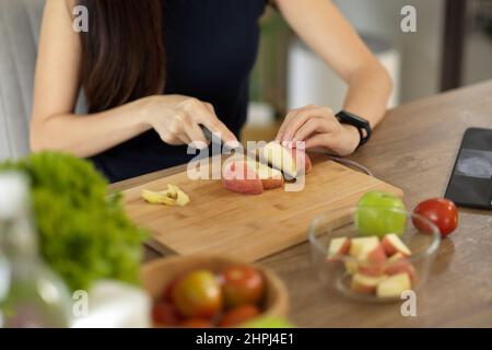 Gros plan, une femme hache des pommes rouges sur une planche à découper, prépare son en-cas diététique sain. Cuisiner à la maison. Banque D'Images