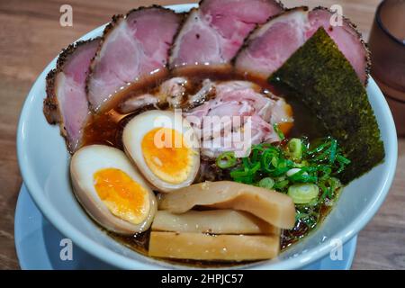 une vue sur le dessus d'un bol en porcelaine rempli de soupe de ramen, servi avec des tranches de porc, de canard salé, de graisse animale, de nori, de saumure marré œuf a mi-bouilli Banque D'Images