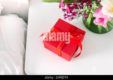 Bouquet de tulipes et boîte cadeau rouge sur la table de nuit près du lit dans la chambre. Concept du jour des femmes, jour des mères Banque D'Images
