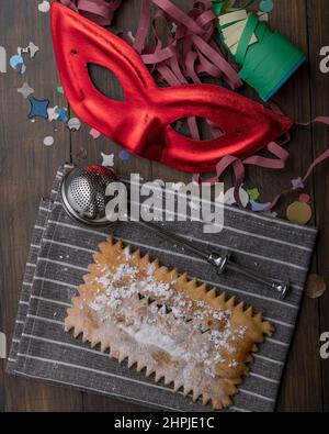 Un dessert typique du carnaval italien de 'chiacchiera', avec du sucre en poudre sur le dessus, un masque rouge, des banderoles et des confettis Banque D'Images