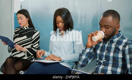 Groupe multiethnique de candidats en attente de commencer une réunion d'entrevue d'emploi, en file d'attente avec cv. Les candidats se préparent à la sélection du recrutement et à une discussion stressante avec les RH. Banque D'Images