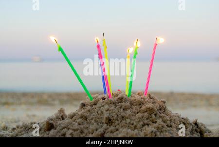 Bougies allumées pour gâteau dans le sable sur fond de vagues de mer floues. Banque D'Images