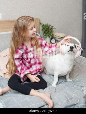 Enfant fille et chien.Une petite fille met des écouteurs sur son chien. Banque D'Images