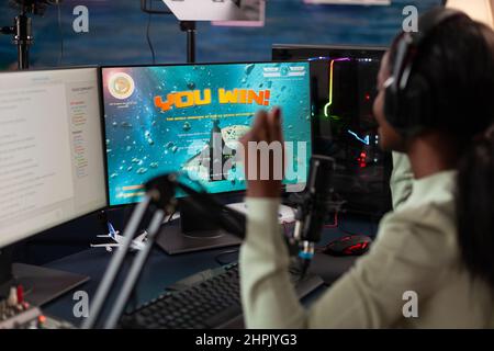 Une joueuse professionnelle excitée gagnante assise au bureau de jeu jouant à des jeux vidéo esport gagnant le championnat en ligne. Diffusion en direct de cyber-joueurs réussie à l'aide d'équipements informatiques RVB. Loisirs Banque D'Images