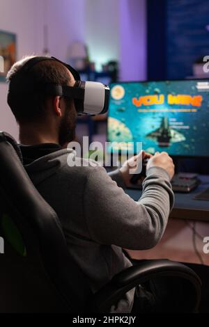 Homme jouant à des jeux vidéo avec joystick et lunettes vr. Joueur gagnant le jeu pendant qu'il utilise le contrôleur et le casque de réalité virtuelle sur l'ordinateur. Le joueur se sent satisfait des gains en ligne. Banque D'Images
