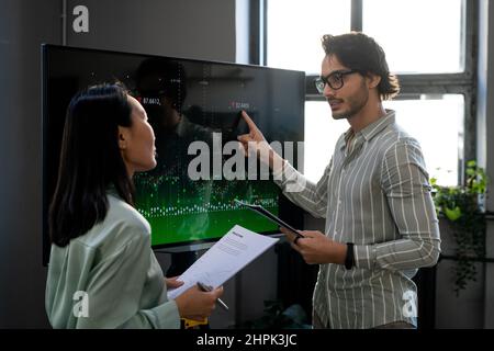 Jeune analyste confiant pointant sur des données financières numériques sur écran interactif pendant la présentation et l'explication à un collègue Banque D'Images