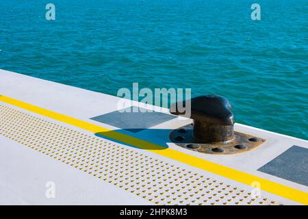 Borne d'amarrage. Un bollard noir amarre sur le quai pour les bateaux de croisière. Ligne jaune de sécurité et pavés tactiles au sol. Banque D'Images
