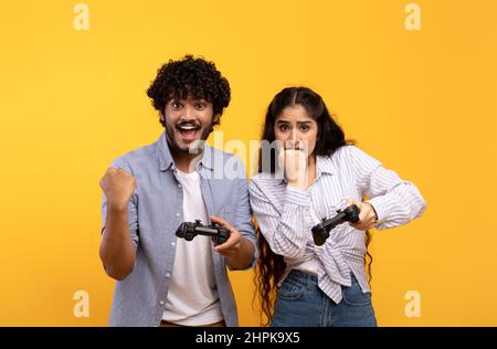 Émotions de la victoire et de la perte dans le jeu en ligne. Un gars indien heureux se réjouissant du succès, près de debout contrarié dame avec joystick Banque D'Images