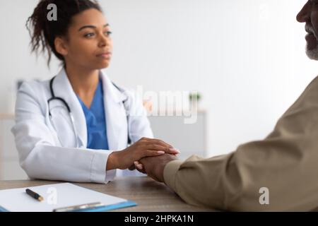 Gros plan d'un médecin de femme noire tenant les mains d'un patient de sexe masculin Banque D'Images