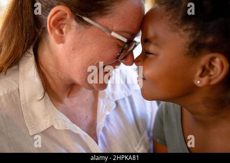 Gros plan sur le sourire de la mère mature du caucase et de la jeune fille afro-américaine qui se frottent le nez Banque D'Images