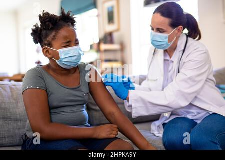 Une femme de race blanche et mature vaccine une fille afro-américaine assise avec des yeux serrés Banque D'Images