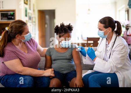 Femme caucasienne mature médecin vaccinant une fille afro-américaine assise par une mère caucasienne mature Banque D'Images