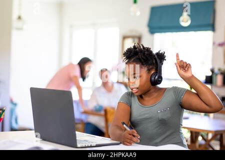 Une fille afro-américaine se levant la main tout en assistant à l'école en ligne sur ordinateur portable à la maison Banque D'Images