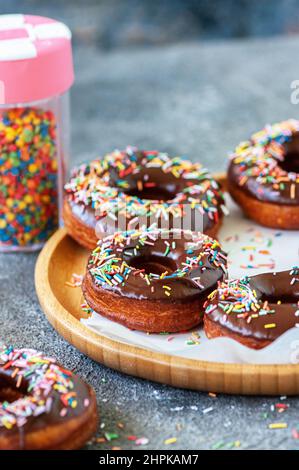 Beignets de chocolat cuits avec des saupoudres colorées sur une assiette en bois. Arrière-plan gris. Banque D'Images