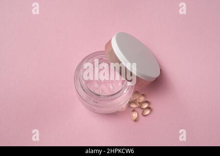Gélofier avec de l'acide hyaluronique dans un pot en verre et des capsules sur fond rose Banque D'Images
