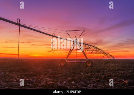 Déplacement latéral système d'irrigation agricole sur le champ labouré au coucher du soleil, équipement agricole pour l'arrosage des terres agricoles cultivées Banque D'Images