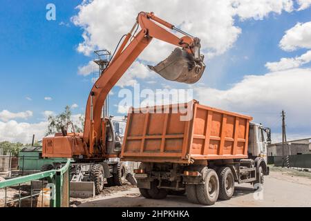 Travaux d'excavation. Le godet du tracteur charge le sol avec une pelle à l'arrière d'un camion-benne sur le chantier. Banque D'Images