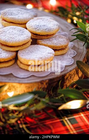 Biscuits de Noël au beurre faits maison sur un plateau en bois dans une table rouge de fête avec des lumières et des herbes Banque D'Images