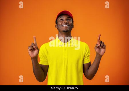 Liveur dans un t-shirt jaune et un chapeau rouge souriant et pointant le doigt vers le haut sur fond orange Banque D'Images