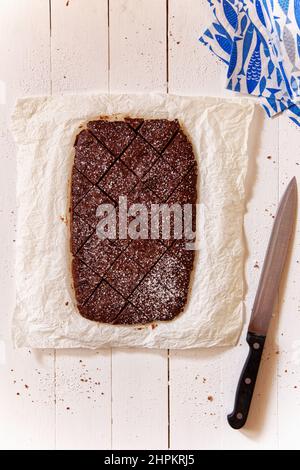 Chocolat au gâteau Choco servi dans du papier de four et de bois blanc couché, couteau et papier bleu fantaisie serviette près, personne, vertical, au-dessus Banque D'Images