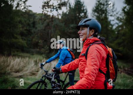 Un couple senior de motards avec des e-bike admirant la nature en plein air dans la forêt en automne. Banque D'Images