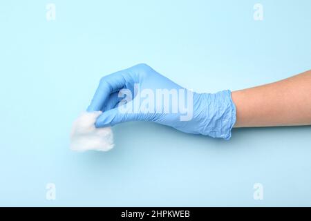 Femme main en caoutchouc gant avec coton laine sur fond bleu, gros plan Banque D'Images