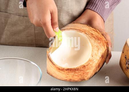 La main féminine déchiquetée la chair de la jeune noix de coco au bol, préparation faisant es Kelapa Muda (glace de la jeune noix de coco) pour le jeûne de Ramadan Banque D'Images