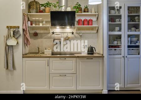 Cuisine moderne beige avec salon dans un intérieur. Armoires blanches avec ustensiles de cuisine et vaisselle Banque D'Images