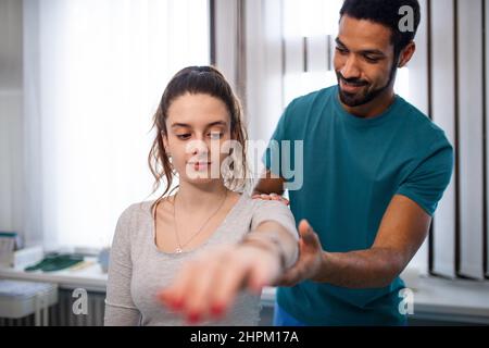 Un jeune physiothérapeute de sexe masculin examine une jeune patiente dans une salle de physiothérapie Banque D'Images