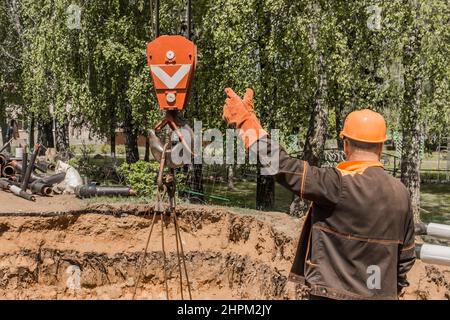 Un travailleur industriel en combinaison et casque de protection prend avec sa main un mécanisme de levage à crochet lourd d'une grue à poutre sur un chantier de construction. Banque D'Images