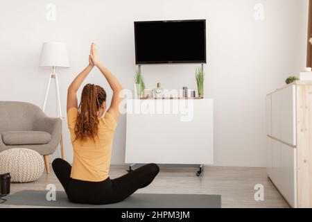 Femme faisant du yoga assis dans la position de Lotus regardant la télévision à l'intérieur Banque D'Images