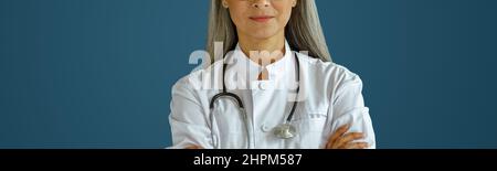 Femme mature médecin en robe avec des lunettes et le stéthoscope se tient sur fond bleu Banque D'Images