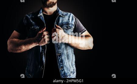 Photo d'un homme en Jean et gilet de motard en denim debout sur fond noir. Banque D'Images