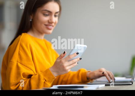 Jolie jeune femme caucasienne utilisant un téléphone portable et un ordinateur portable pour un travail en ligne ou des études à la maison, l'espace de copie Banque D'Images