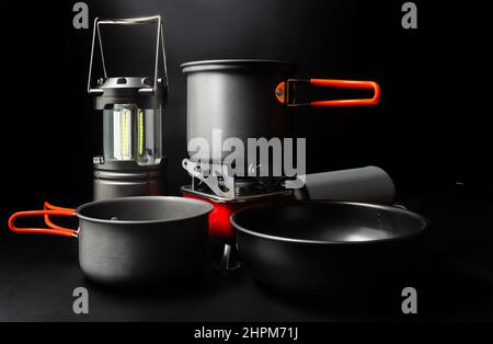 Photo d'ustensiles de camping en titane avec lanterne LED et cuisinière à gaz portable sur fond noir. Banque D'Images