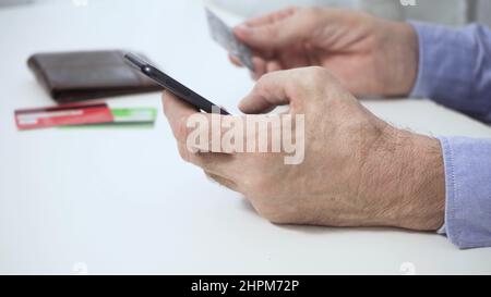 Les mains d'un homme qui, en tenant un smartphone, une carte de crédit, effectue un paiement réussi. Banque D'Images