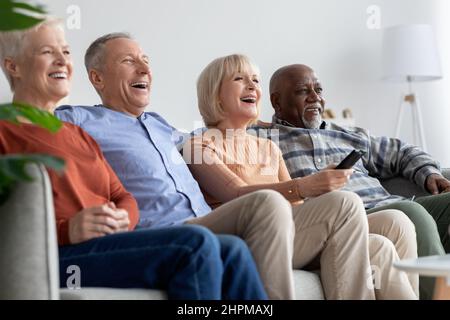 Amis multiraciaux personnes âgées regardant la télévision et riant Banque D'Images