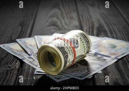 Un rouleau de billets et de pièces de monnaie en dollars sur d'autres billets sur un bureau. Mettez en surbrillance pour la facture de cent dollars. Un épais rouleau de vieux billets de cent dollars liés Banque D'Images