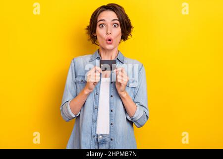 Photo de jeune fille impressionnée boutique dépenser beaucoup d'argent tenir carte de crédit isolée sur fond jaune de couleur Banque D'Images