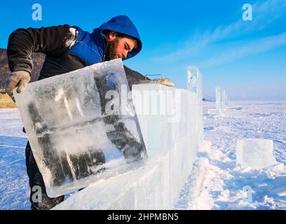 18 février 2022 Russie, Listvyanka. Un sculpteur construit un mur à partir d'un bloc de glace sur le lac Baikal. Banque D'Images