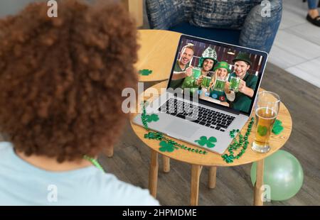 Homme de course mixte au bar pendant la journée de St patrick, appel vidéo à des amis en costumes buvant sur un ordinateur portable Banque D'Images