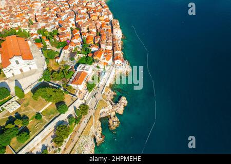 Toits rouges lumineux de bâtiments dans la ville de Rowinj sur la péninsule dans la mer Adriatique. Vieille ville croate traditionnelle avec des arbres verts à la lumière du soleil. Vue aérienne Banque D'Images