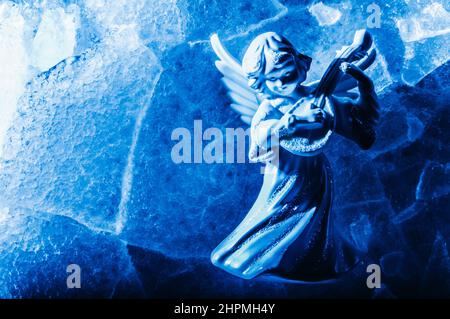 Photo en gros plan d'ange de glace bleu en miniature jouant le luth et posant sur fond de glace craquée. Banque D'Images